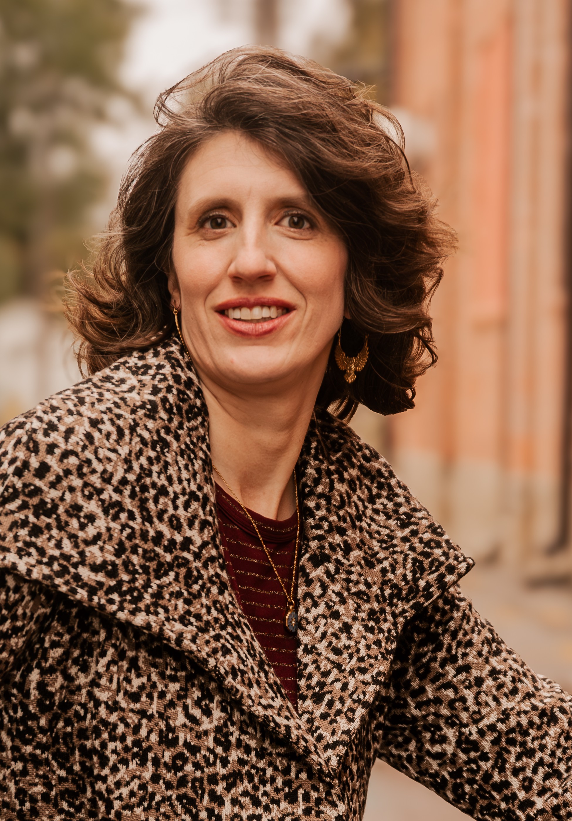 Katharine Ragon, a women with curled, brown, shoulder length hair wearing an animal print blazer